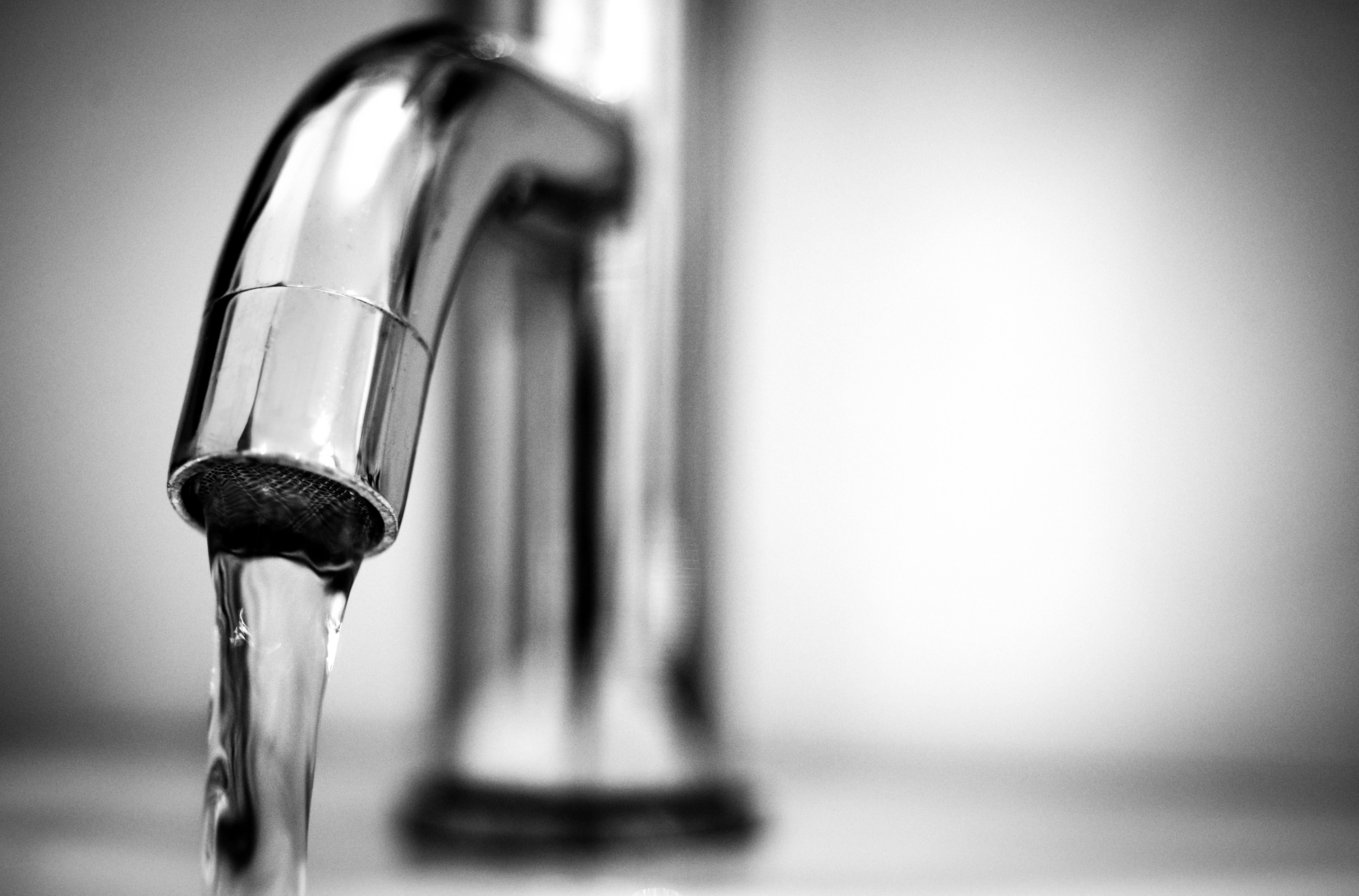 A black-and-white close-up of water flowing from a stainless steel faucet.