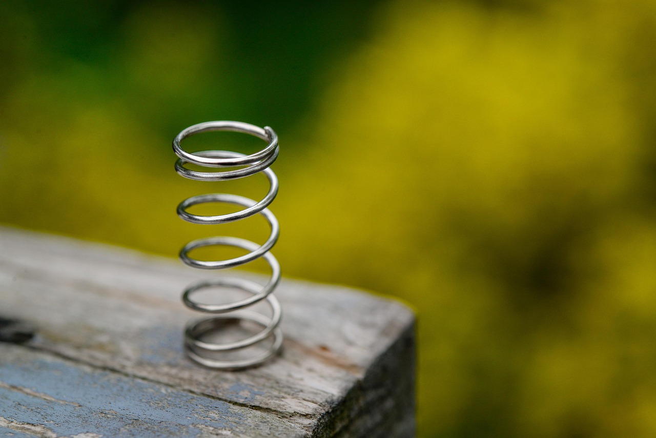 A single steel coil spring stands upright on a wooden surface.