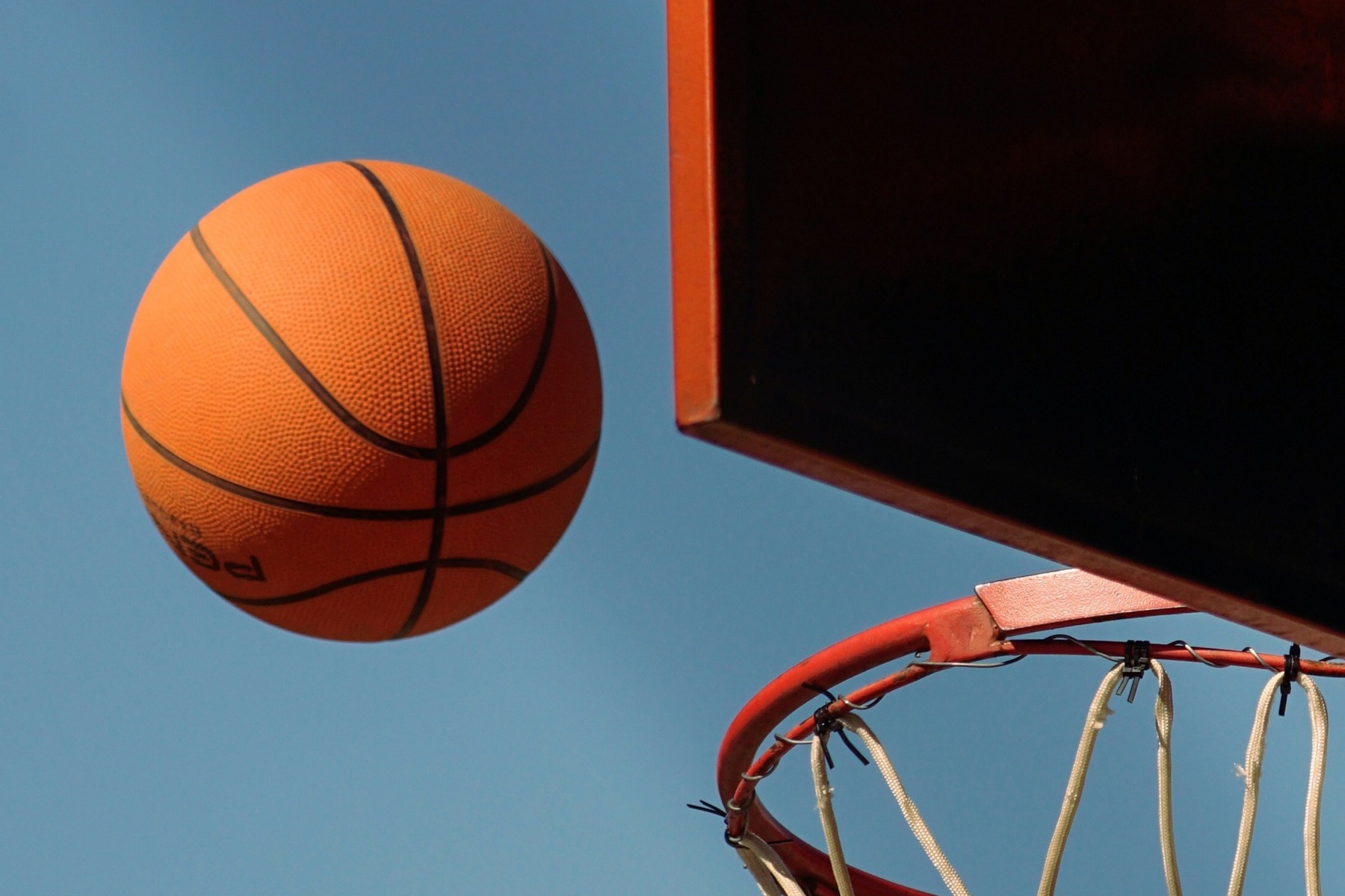 A basketball suspended in the air beside an outdoor hoop