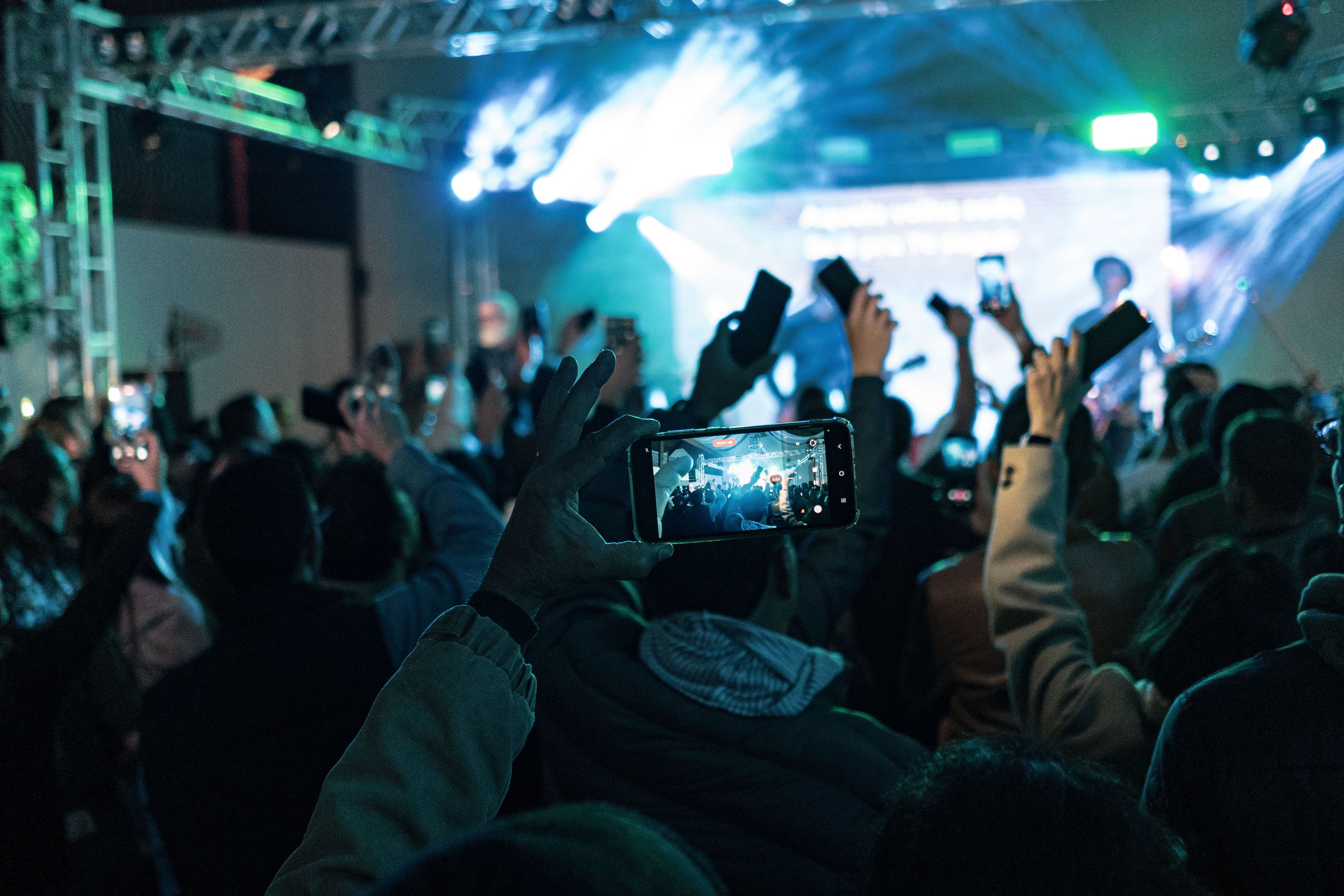 Concertgoers hold up phones to record a brightly lit stage