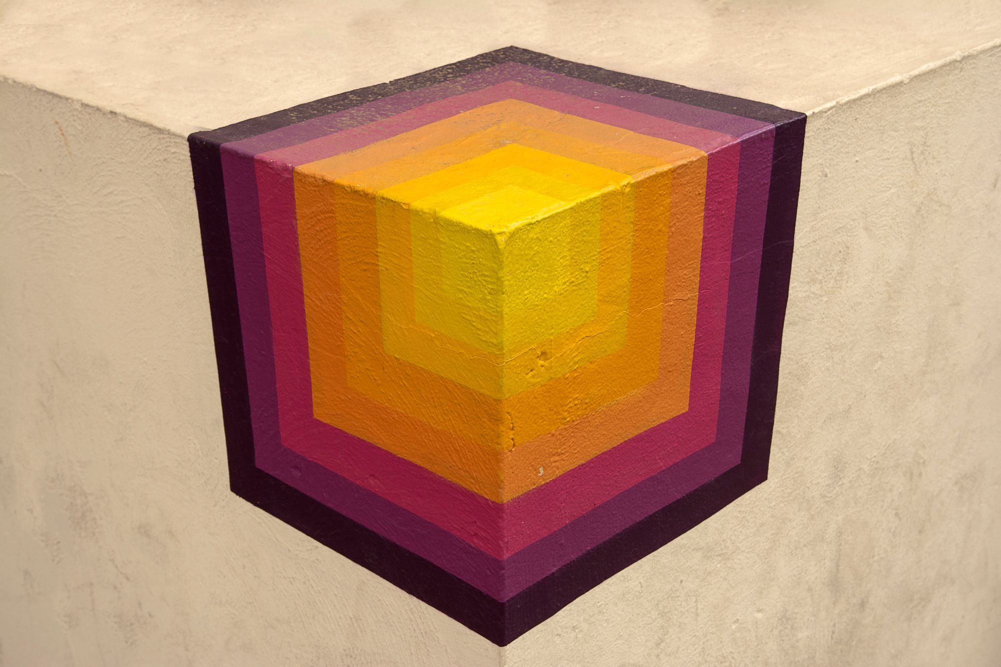 A colorful geometric mural of interlocking cubes painted around the corner of a concrete wall.